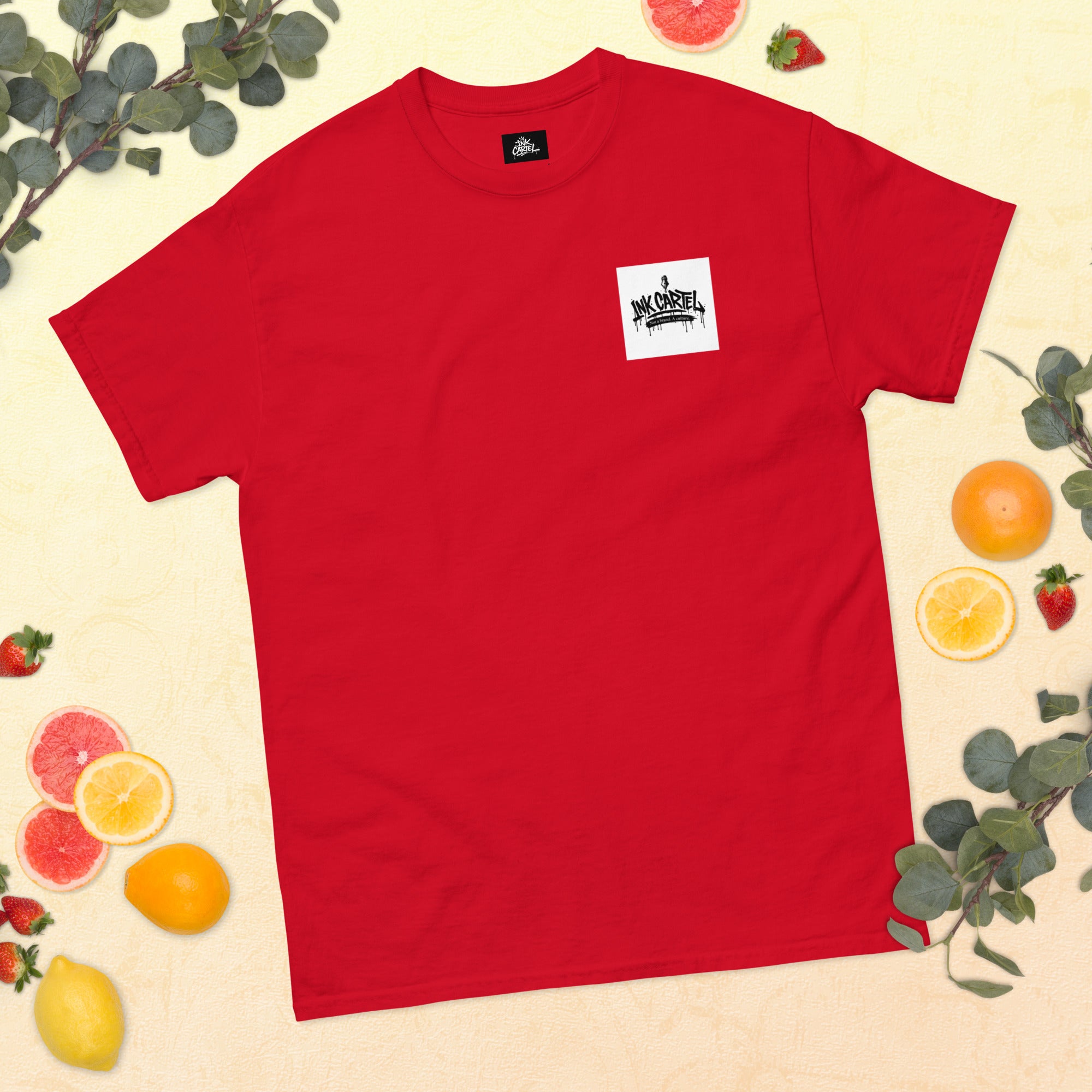 Red t-shirt with a small logo on a beige background with fruits and leaves.